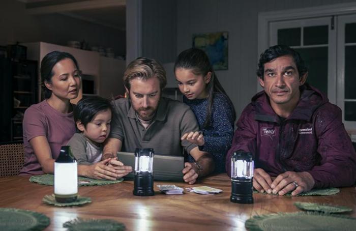 Johnathan Thurston sitting with a family in a house with no power. The family is creating a plan on a tablet.