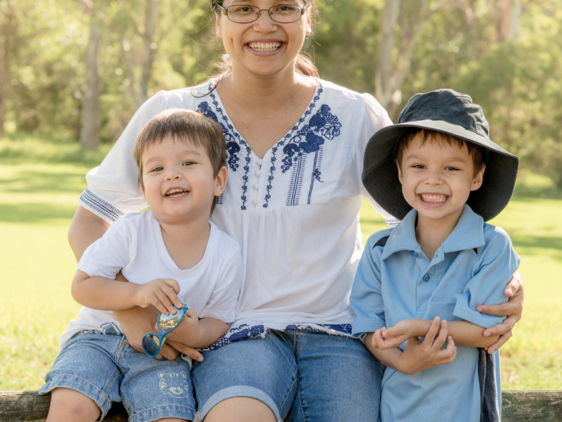 Mother sitting outside on a wooden picnic bench with her two primary-aged children..